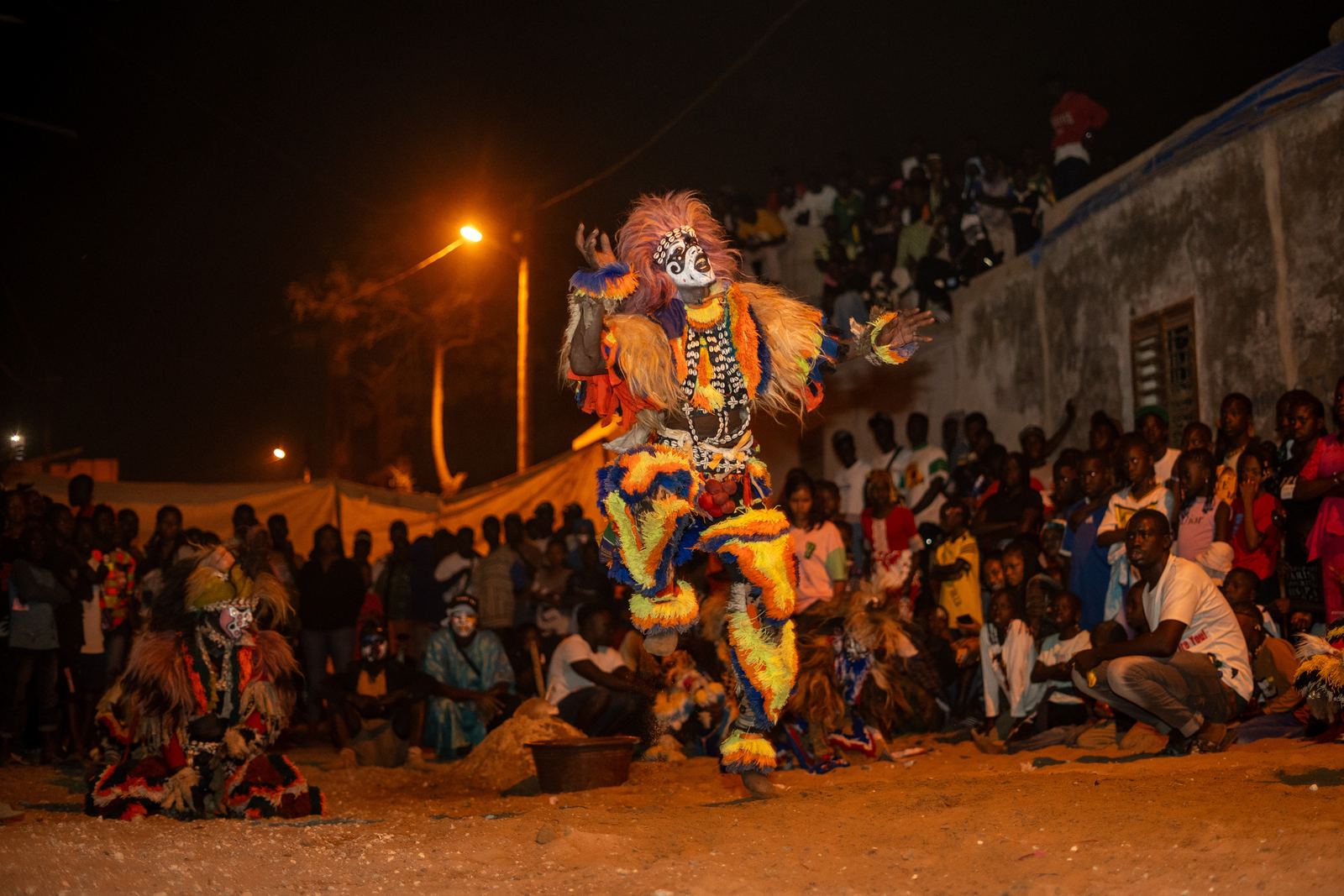 A masked dancer in a fibre costume performing at night before a crowd