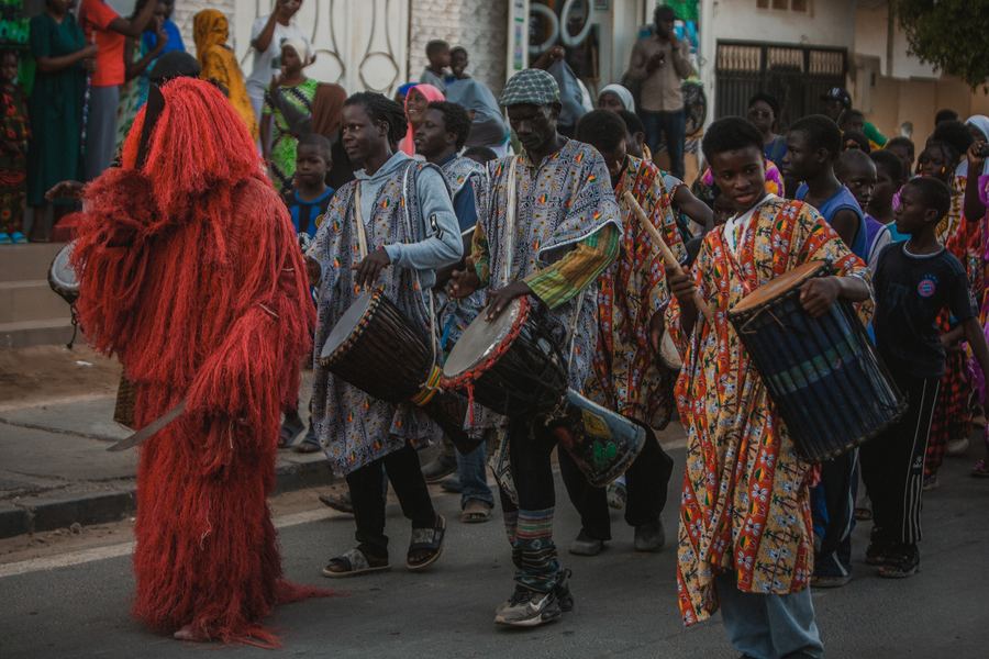 Drummers and a masked figure in red fibre leading a street procession