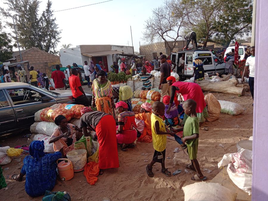 A village market with traders, sacks of produce and children playing